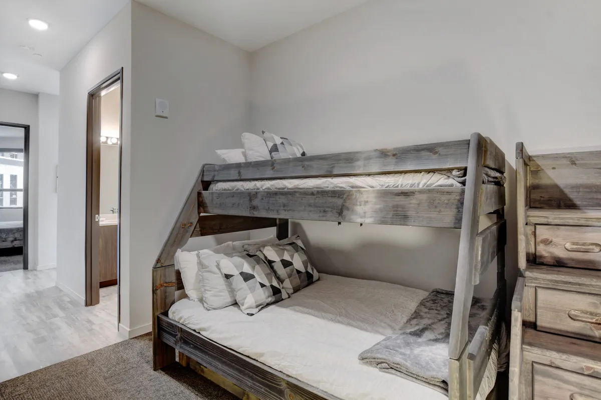 A playful bunk room with a sturdy full and twin bunk bed, soft, textured bedding, and decorative pillows. The space is designed for versatile family sleeping arrangements and cozy gatherings, with an inviting, relaxed mood.