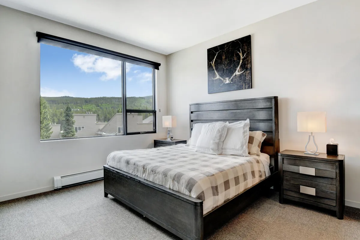 A serene bedroom featuring a comfortable bed with premium bedding, a large window that floods the space with natural light, and tasteful artwork on the wall. The peaceful, uncluttered setting evokes a sense of relaxation and rest.