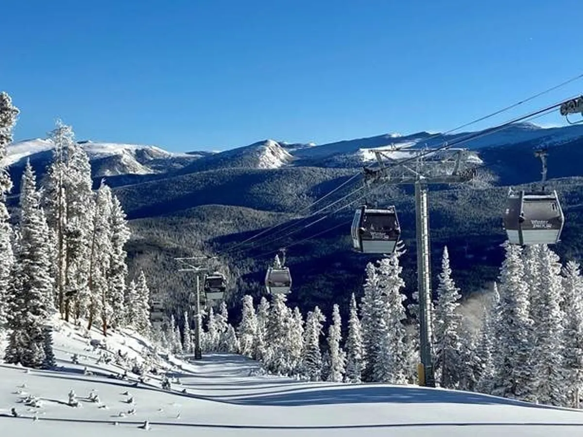 A sweeping winter landscape featuring snow-covered ski slopes, a gondola lift ascending the mountain, pine trees dusted with snow, and distant mountain peaks. The scene conveys both excitement and tranquility, perfect for ski-in/ski-out convenience.