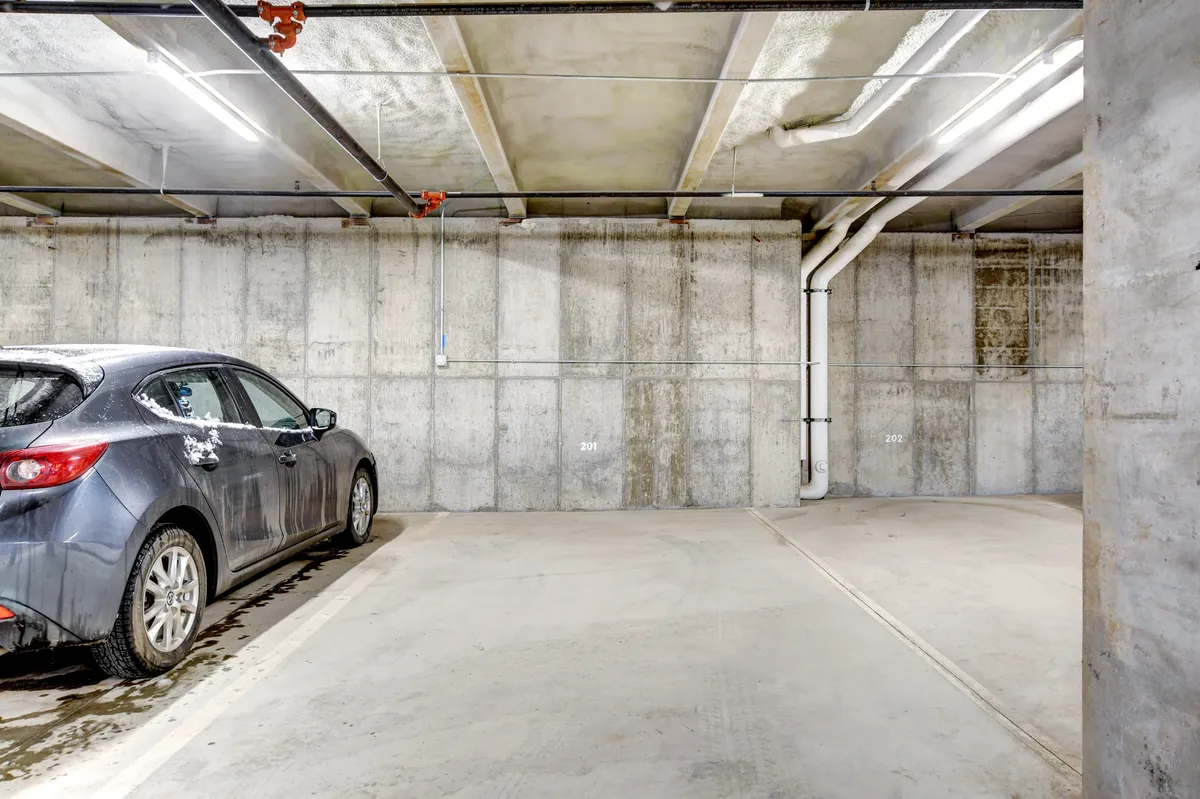 This image features a parked car inside a concrete parking garage, with overhead lighting illuminating the space. The scene conveys the practicality and limited nature of the on-site parking available to guests.