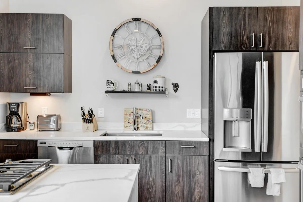 A modern kitchen equipped with sleek appliances and cabinetry, accented by a decorative wall clock. The space is clean, organized, and practical for family gatherings or everyday cooking, aligning with the convenience and functionality described in the section.