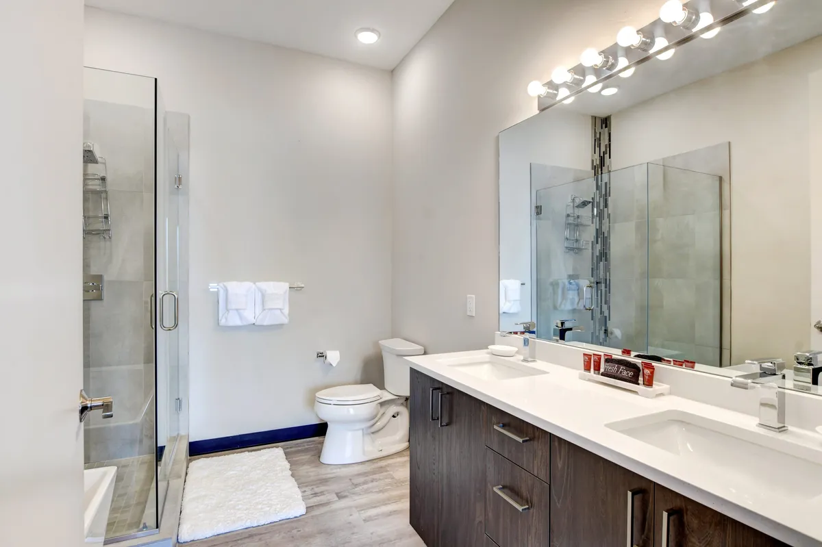 A calming bathroom with a double sink vanity, a walk-in shower, and a large mirror. The space feels serene and well-equipped, echoing touches like organic bath products and plush essentials mentioned in the text.