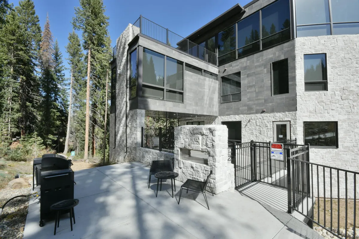 A modern exterior featuring a grill area, comfortable outdoor seating, and lush surrounding trees. The inviting setup is perfect for couples to unwind, host a sunset barbecue, or stargaze together in a peaceful mountain environment.