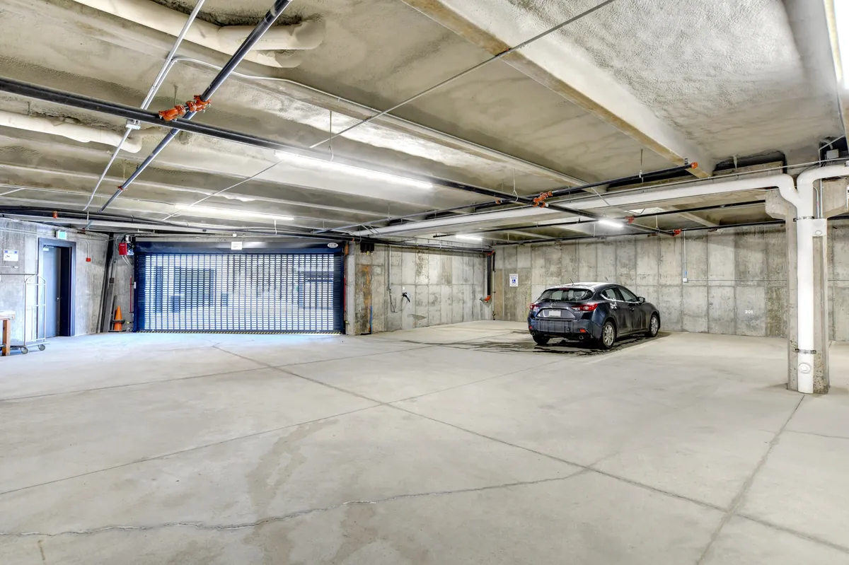 A secure, heated underground parking area with a single car parked, visible security gate, and concrete walls. The space exudes practicality and safety for guests arriving by vehicle.