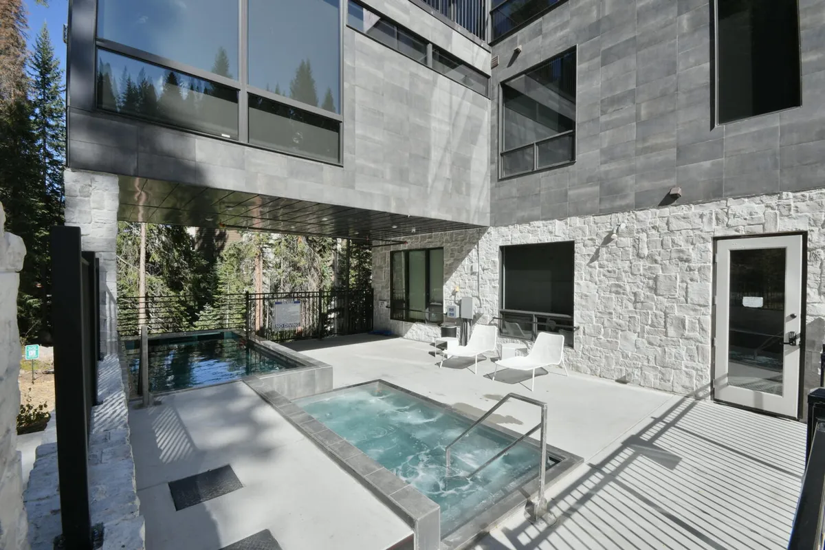 An inviting outdoor hot tub and swimming pool nestled among modern architecture and surrounded by trees. The area offers relaxation options with mountain views, perfect for unwinding after a day of adventure.