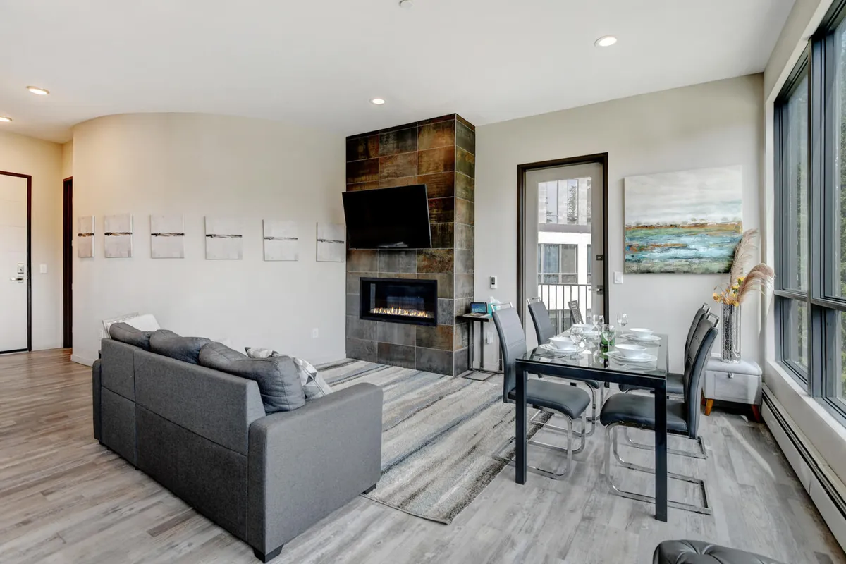A cozy living room scene featuring a custom gas fireplace, a plush sofa, a dining table, and tasteful artwork. The space is designed for relaxation and entertaining, with warm lighting and a welcoming layout that encourages gathering and conversation.