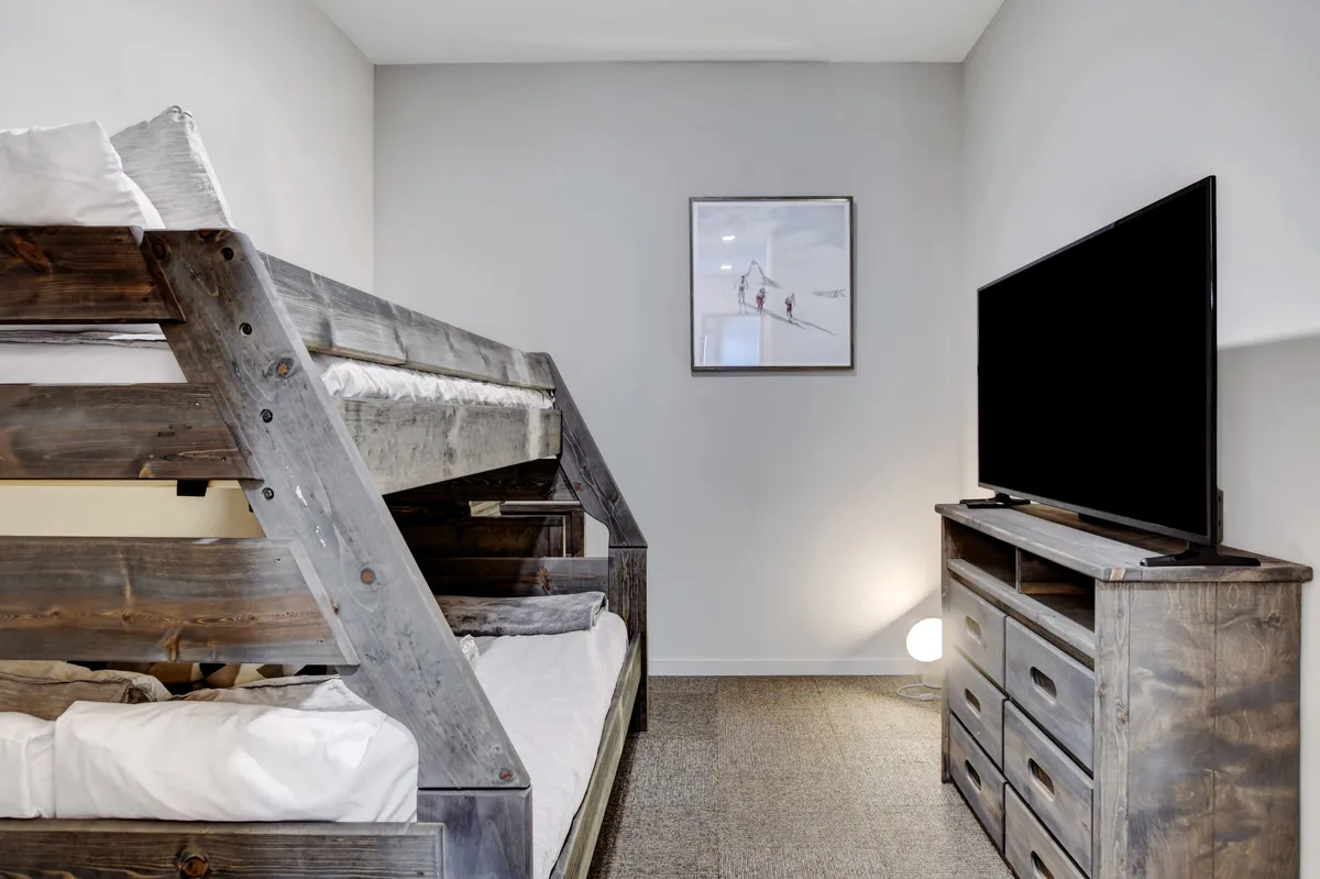 A cozy bedroom featuring a bunk bed, TV, wooden dresser, and playful artwork. The decor creates a comfortable, relaxed vibe perfect for children or teens, reflecting the flexible sleeping arrangements that support families of all ages.