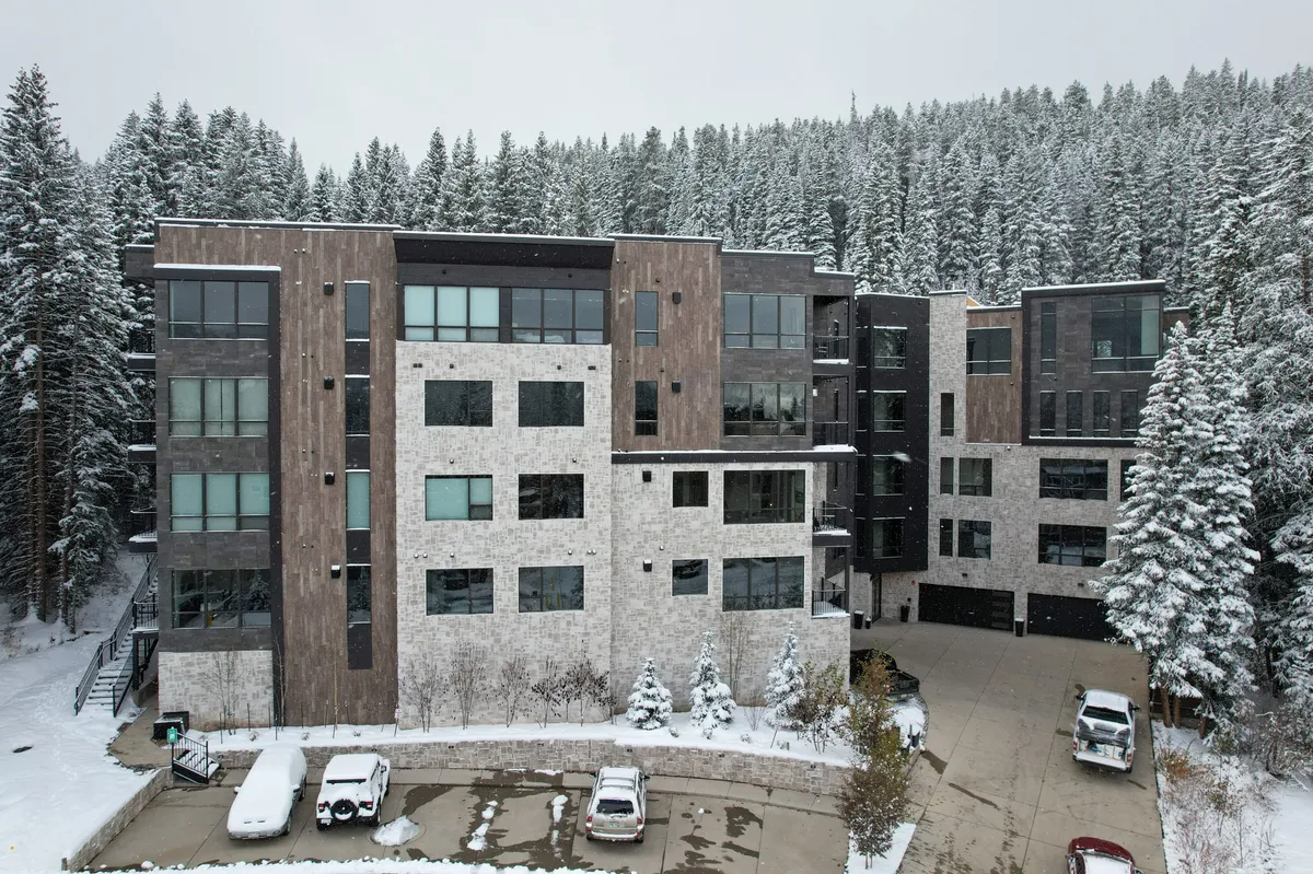 A picturesque exterior shot of the resort's modern architecture set among snow-covered trees, with parked cars hinting at easy access and family arrivals for a winter retreat.