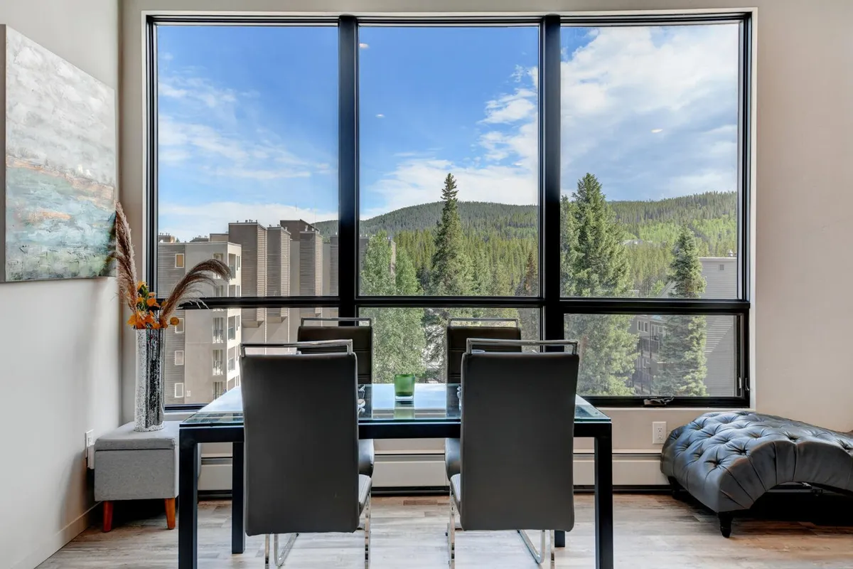 A spacious dining area with large windows, a dining table, and decorative plants, offering a stunning view of the surrounding mountains. The natural light and inviting setup hint at the connection between indoor comfort and the beauty of the outdoors.